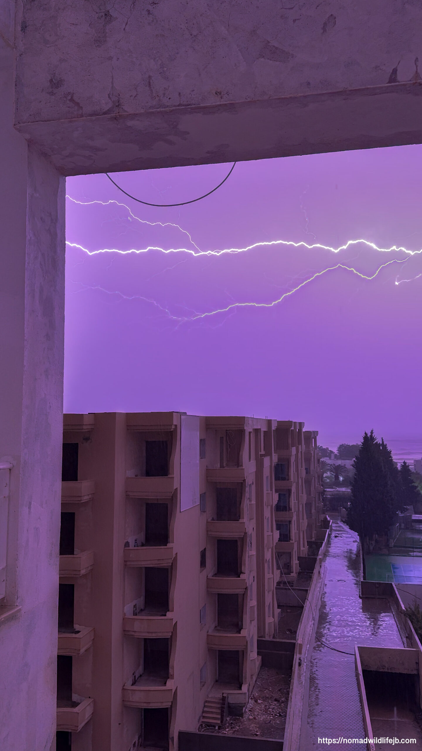 Horizontal lightning stretching across a purple storm sky above apartment buildings during a severe thunderstorm in Hammamet, Tunisia.