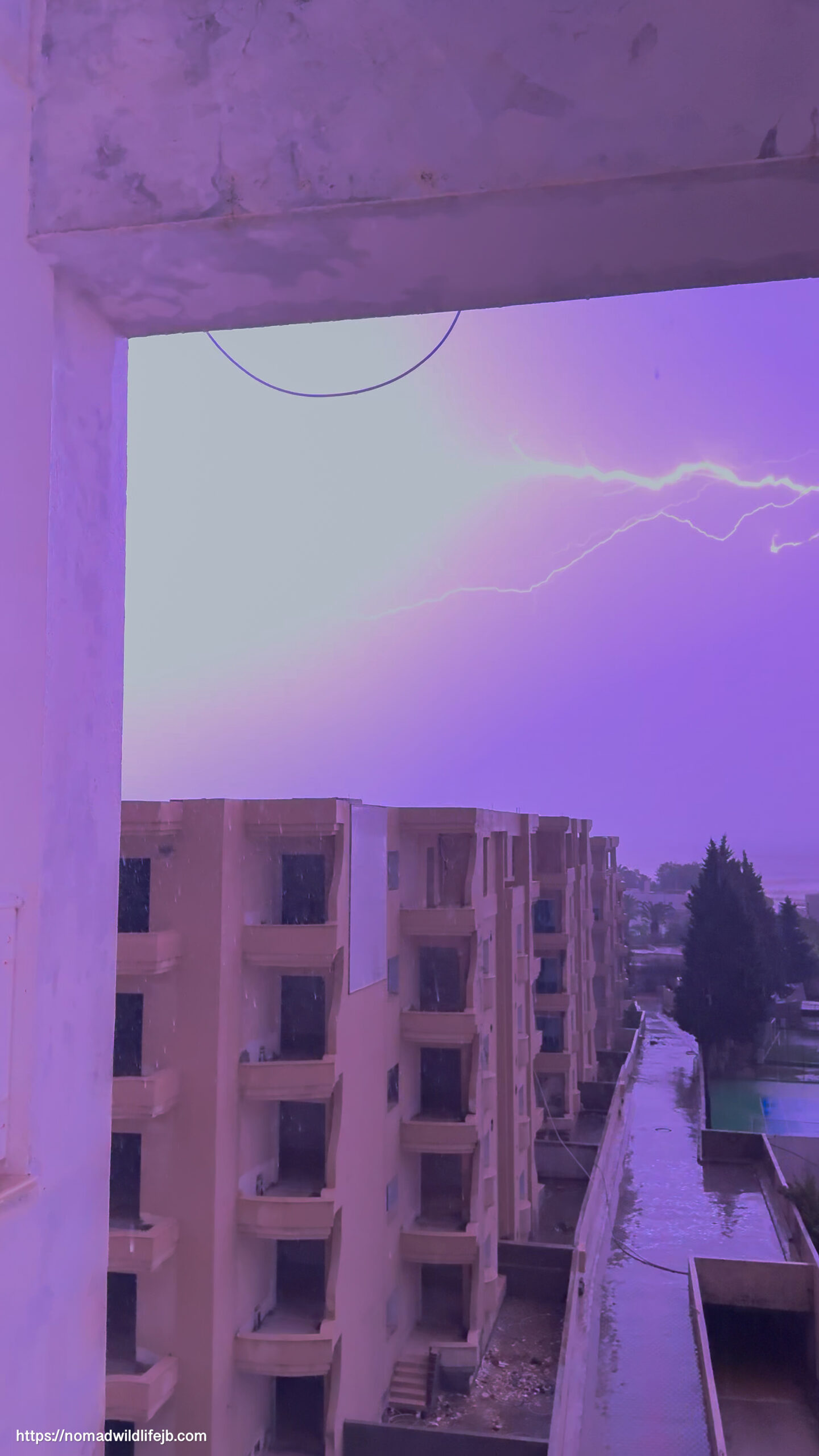Sideways lightning cutting across a purple-lit storm sky above apartment buildings in Hammamet