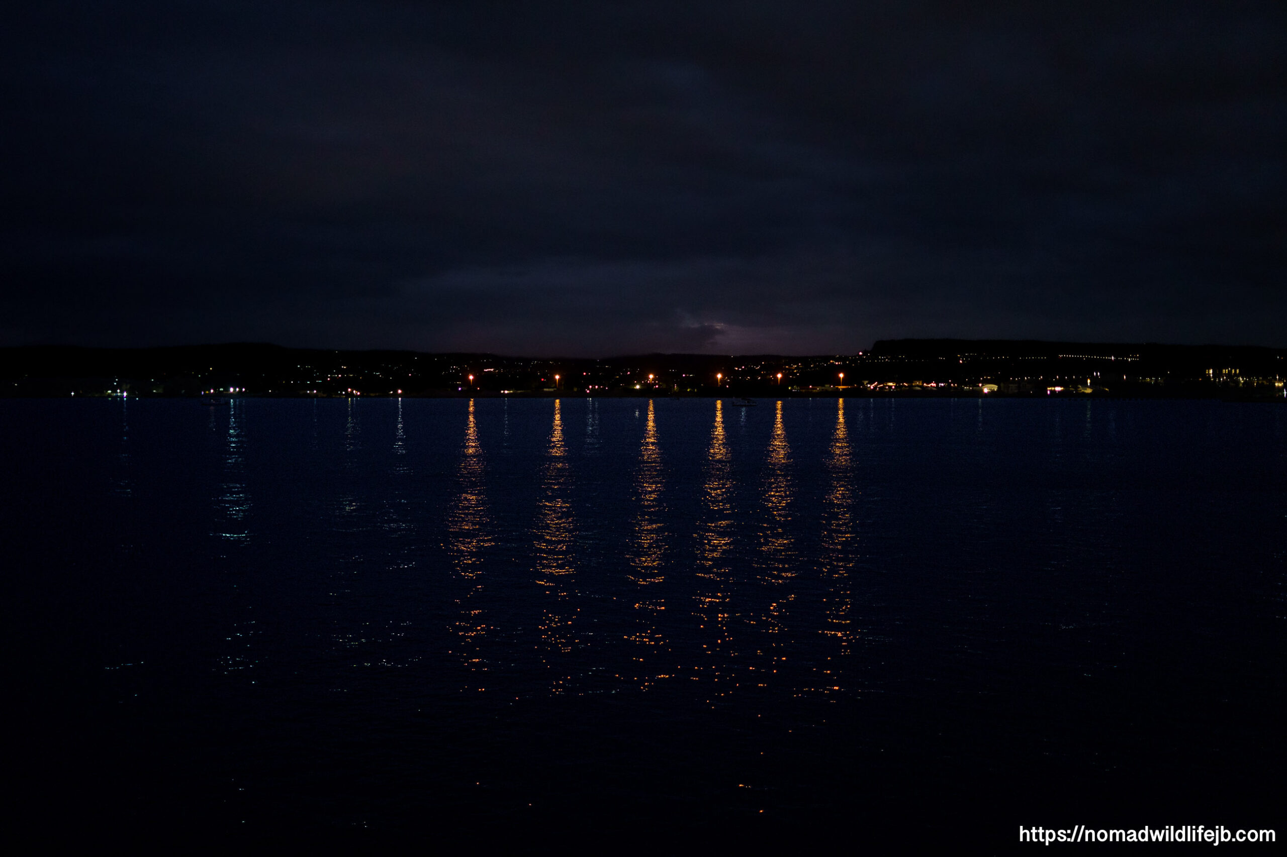 City lights reflecting on the water of the Mediterranean Sea at night near Syracuse, Sicily