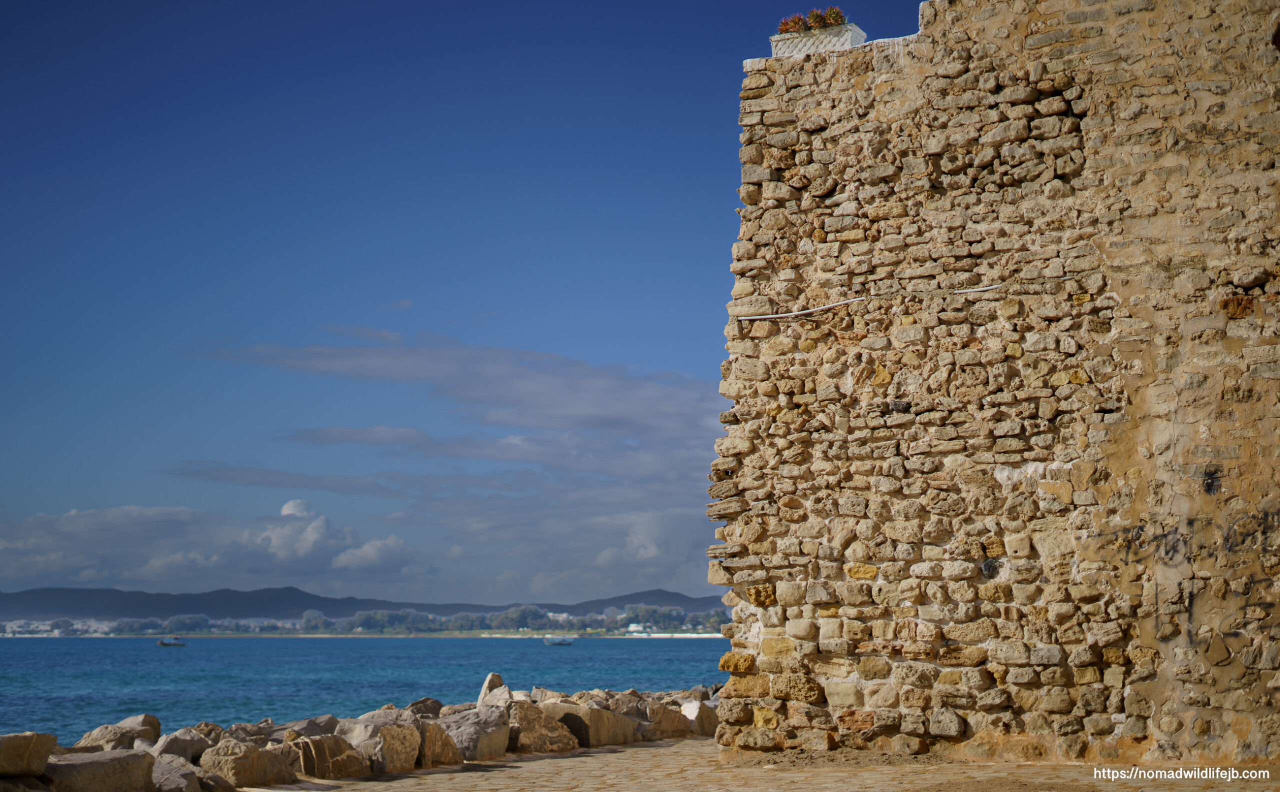 Stone fort wall on the coast with blue sea and sky in Hammamet, Tunisia.