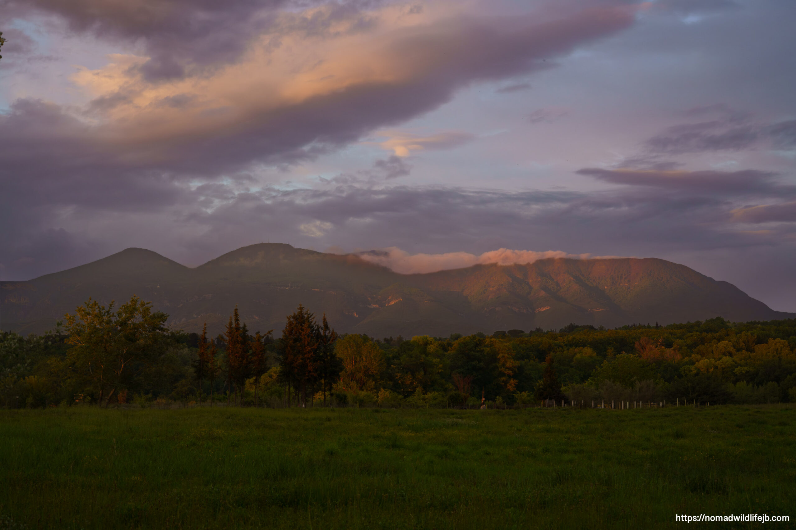 Golden hour light illuminates mountains beyond Tirana Lake as evening clouds drift across the sky in Albania.