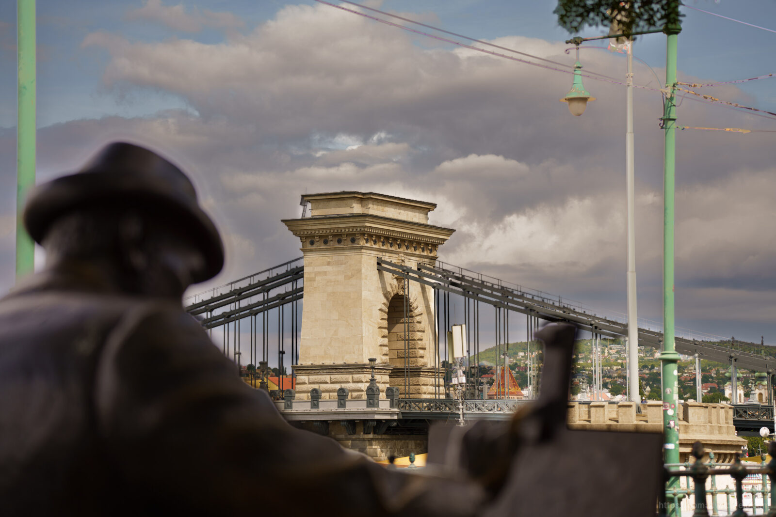 Budapest's Chain Bridge framed by bronze statues beneath a cloudy sky along the Danube River.