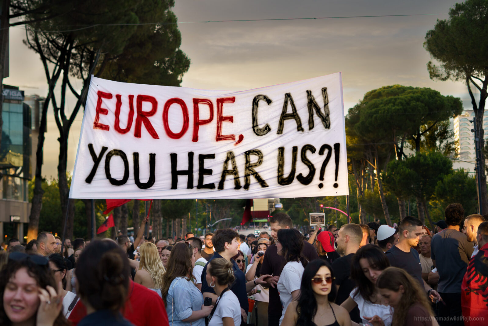 Protesters in Tirana gather beneath a large banner reading “Europe, can you hear us?”