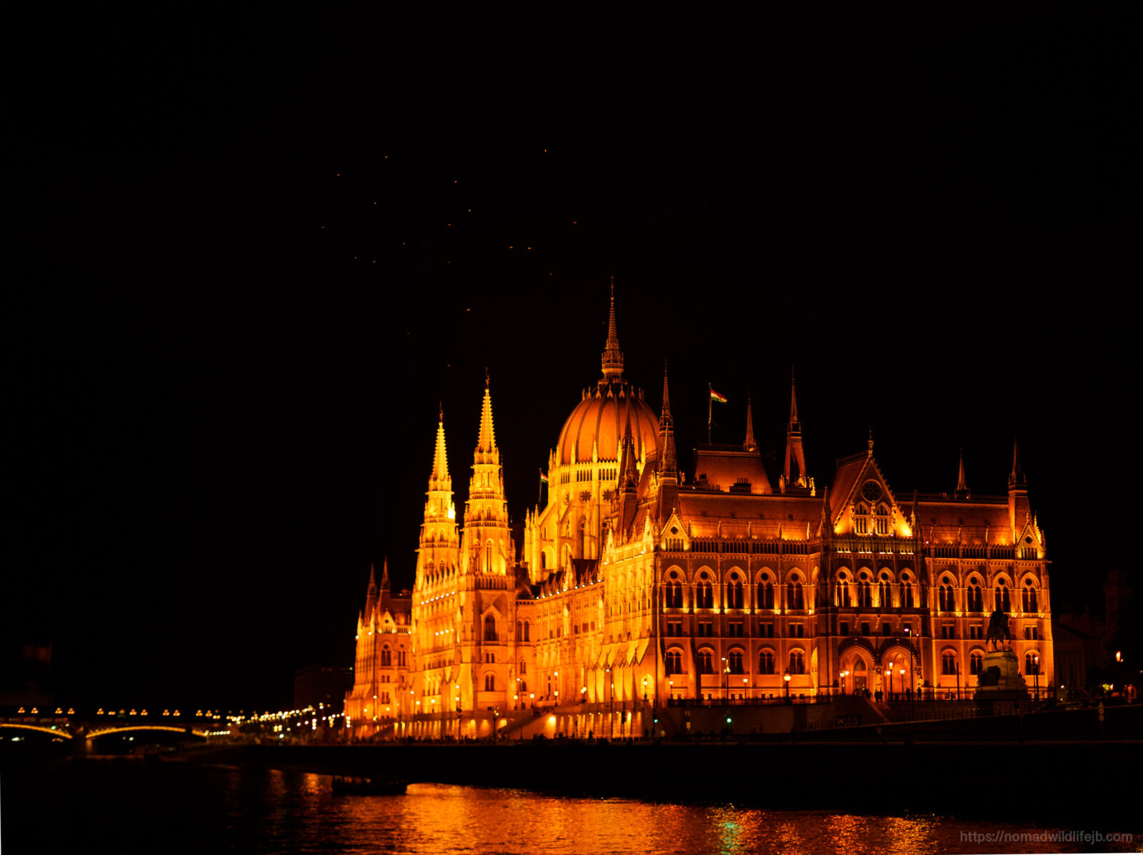 Hungarian Parliament Building illuminated at night beside the Danube River in Budapest.